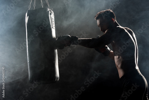 silhouette of athlete in boxing gloves hitting punching bag on black with smoke