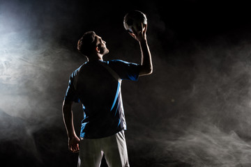 silhouette of player in uniform holding ball above head on black with smoke