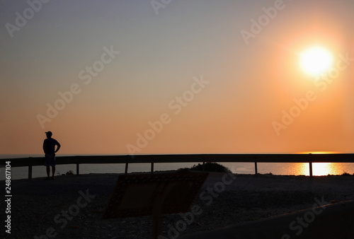 Sunset over the sea and road, traffic devider and dark silhouette of man with cap on his head,, Horizontal. Mideterranian, cyprus, road, ecology. With copy space