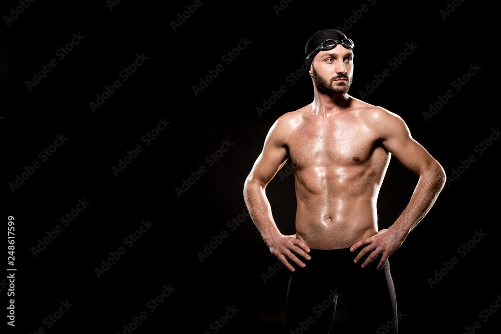 Fototapeta premium muscular swimmer standing in swimming cap and swim goggles isolated on black