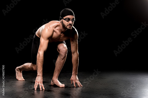 muscular swimmer standing in start position on black background