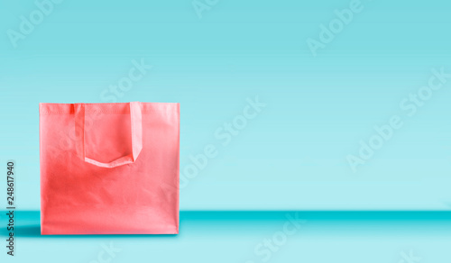 Shopping bag in living coral color standing on table at turquoise wall background. Branding mock up. Copy space. Purchase , sale and promotion concept. Banner or template. Creative layout