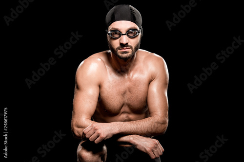 handsome swimmer sitting in swimming cap and goggles isolated on black