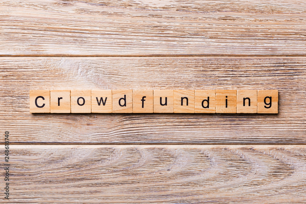 Fototapeta premium CROWDFUNDING word written on wood block. CROWDFUNDING text on wooden table for your desing, concept