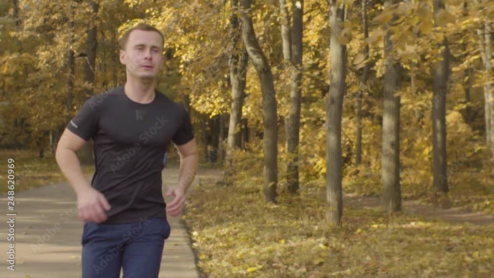 Slow motion of man in sportswear running along road in the park. Dolly shot Slow motion of man in sportswear running along road in the park. Dolly shot