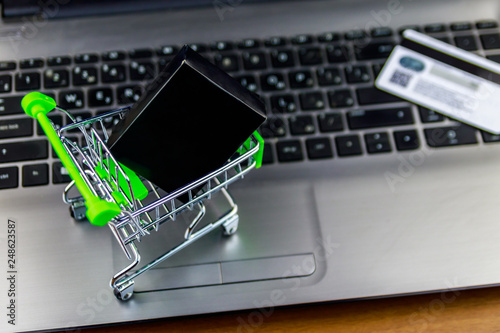 Online shopping concept. Small shopping cart with box and credit card on laptop keyboard