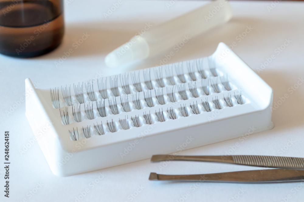 Eyelash extension, beauty and cosmetology concept - set of false eyelashes, glue and tweezers on white table Eyelash extension, beauty and cosmetology concept - set of false eyelashes, glue and tweezers on white table