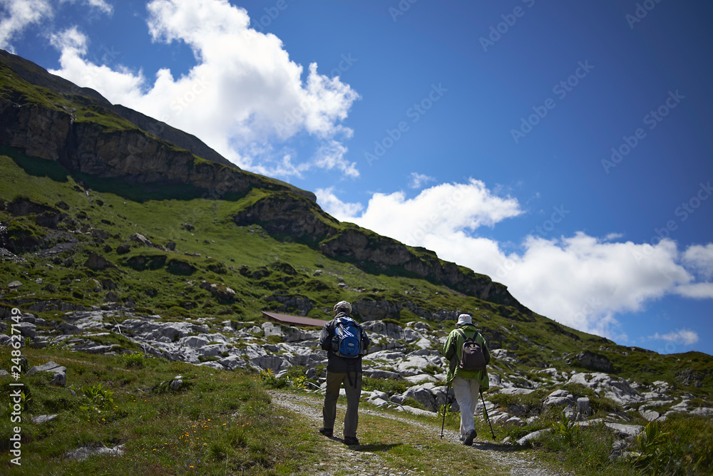 Elderly couple hiking up a mountain path in the Swiss Alps in summer sunshine