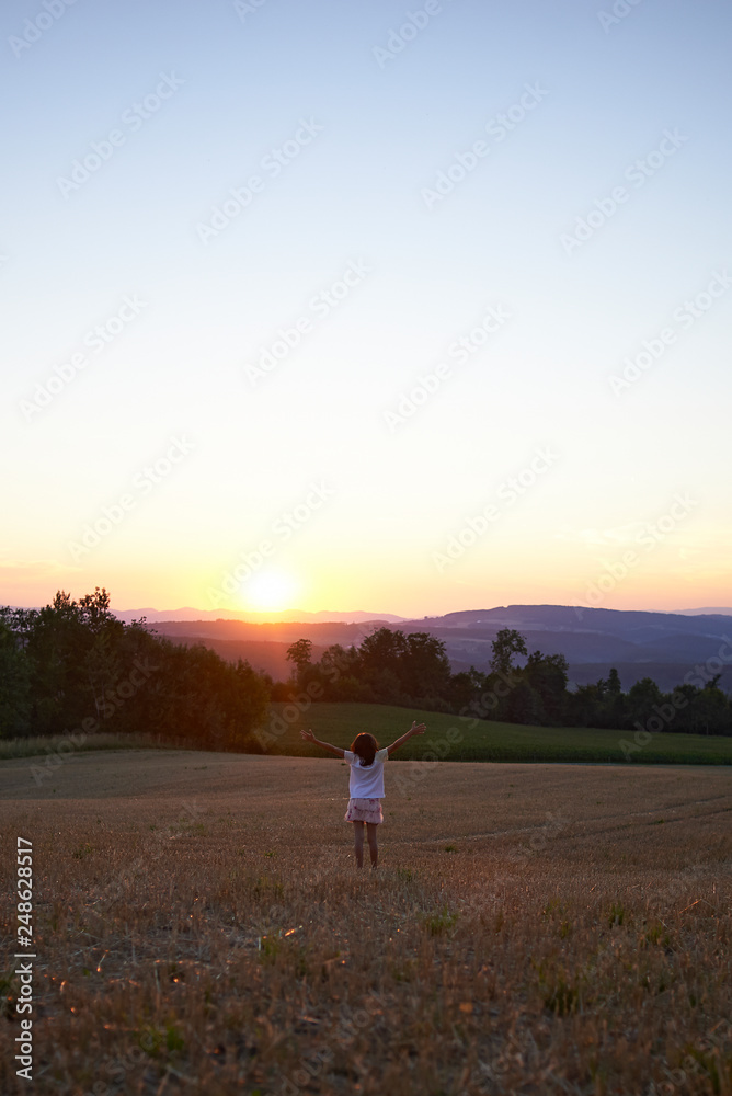 Beautiful classic shot of a little girl in a white dress walking on the hills of a field in spring sunset Beautiful classic shot of a little girl in a white dress walking on the hills of a field in spring sunset