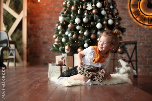 curious little girl sitting near the Christmas tree .