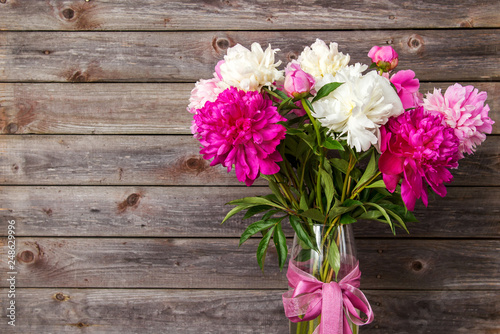 bouquet of pink and white peony flowers in a vase on a wooden ba