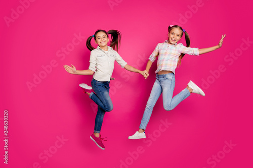 Full length body size photo two little age she her girls hand arm jump high win school competition cheerleaders wear casual jeans denim checkered plaid shirts isolated pink vibrant vivid background