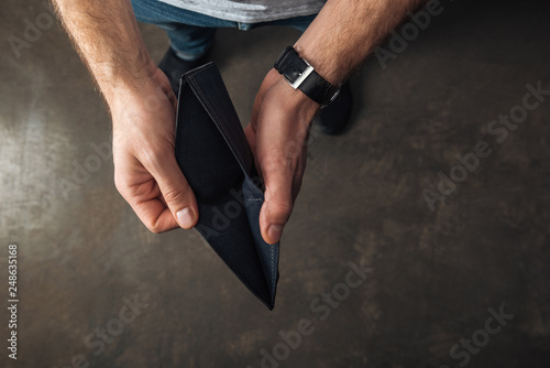 top view of man holding empty wallet on dark background