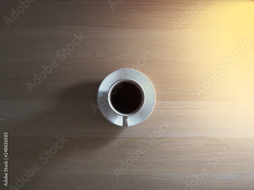 Black coffee, white cup on the table, wood grain in the top view, with golden light shining from the side
