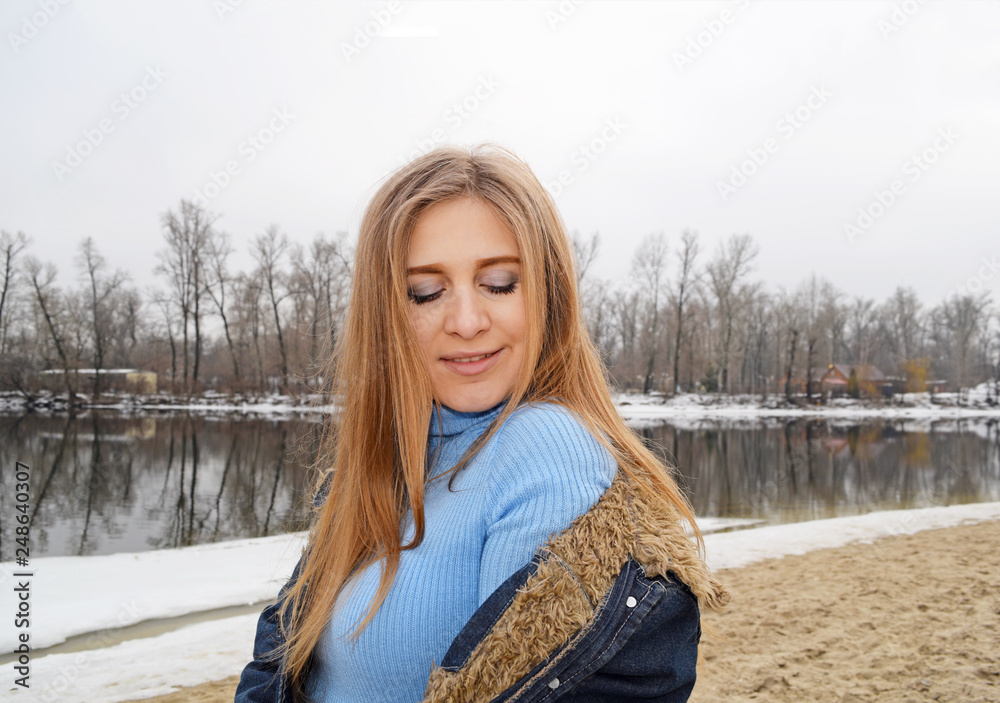 Portrait of a girl with closed eyes in a sweater and jacket near the river in the winter. Portrait of a girl with closed eyes in a sweater and jacket near the river in the winter.