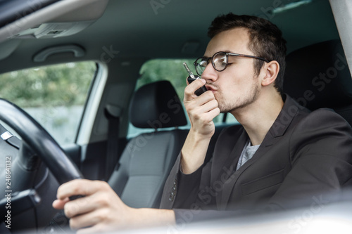 Satisfied young man is kissing his car keys while sitting at the car. His left hand is on the steering wheel. © Maksym
