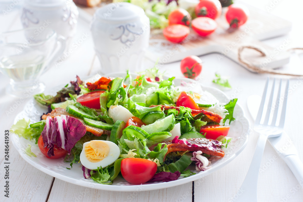 Fresh salad of roasted bacon, cherry tomatoes, quail eggs on a white plate, horizontal Fresh salad of roasted bacon, cherry tomatoes, quail eggs on a white plate, horizontal