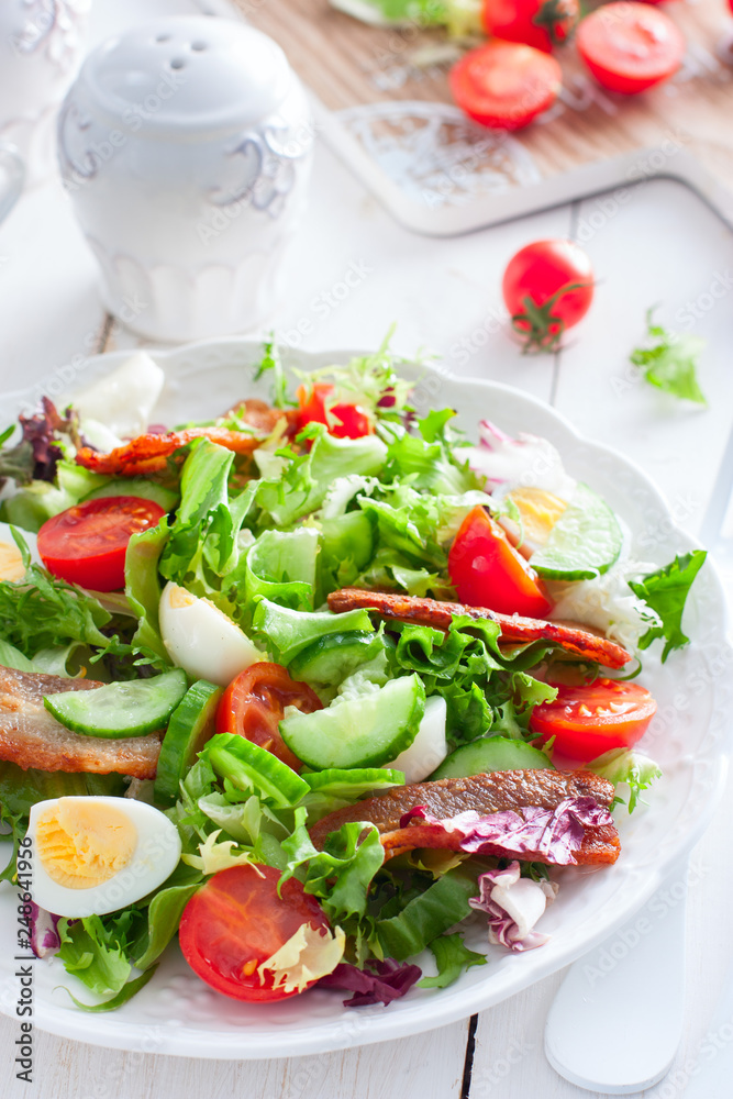 fresh salad of roasted bacon, tomatoes and eggs on a white plate, selective focus