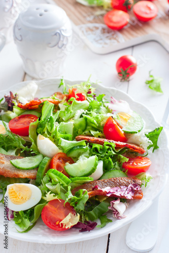 fresh salad of roasted bacon, tomatoes and eggs on a white plate, selective focus