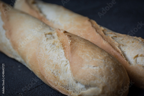 Macro view of freshly baked crunchy baguette bread on dark background. Closeup of crust of bread food background. Natural lighting