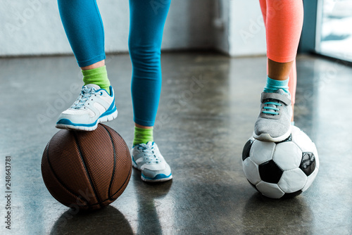 Cropped view of kids in sneakers posing with balls in gym