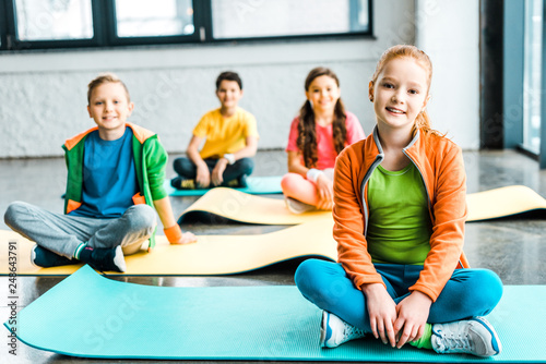 Children sitting on fitness mats and looking at camera with smile