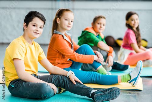 Cheerful preteen kids sitting on mats in gym