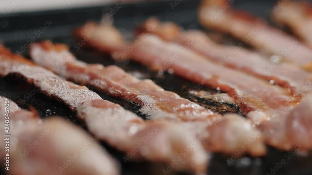 Bacon slices frying over a stove. Camera moving slowly over a close-up view of bacon slices with frying over a stove. Bacon slices frying over a stove. Camera moving slowly over a close-up view of bacon slices with frying over a stove.