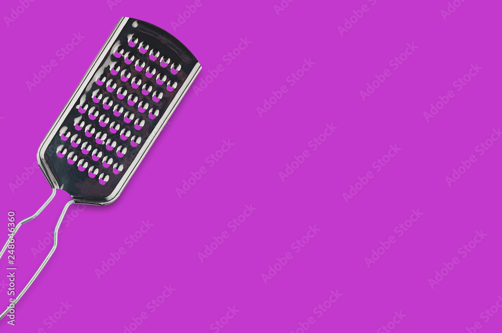 One glossy metallic rectangular sharp grater for different foodstuff on purple table on kitchen with copy space for your text. Top view. Cooking concept One glossy metallic rectangular sharp grater for different foodstuff on purple table on kitchen with copy space for your text. Top view. Cooking concept