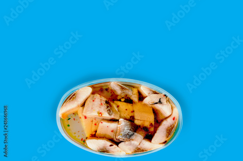 One oval transparent plastic container of canned seafood and spice in marinade on blue table on cuisine with copy space for your text. Top view. Breakfast concept