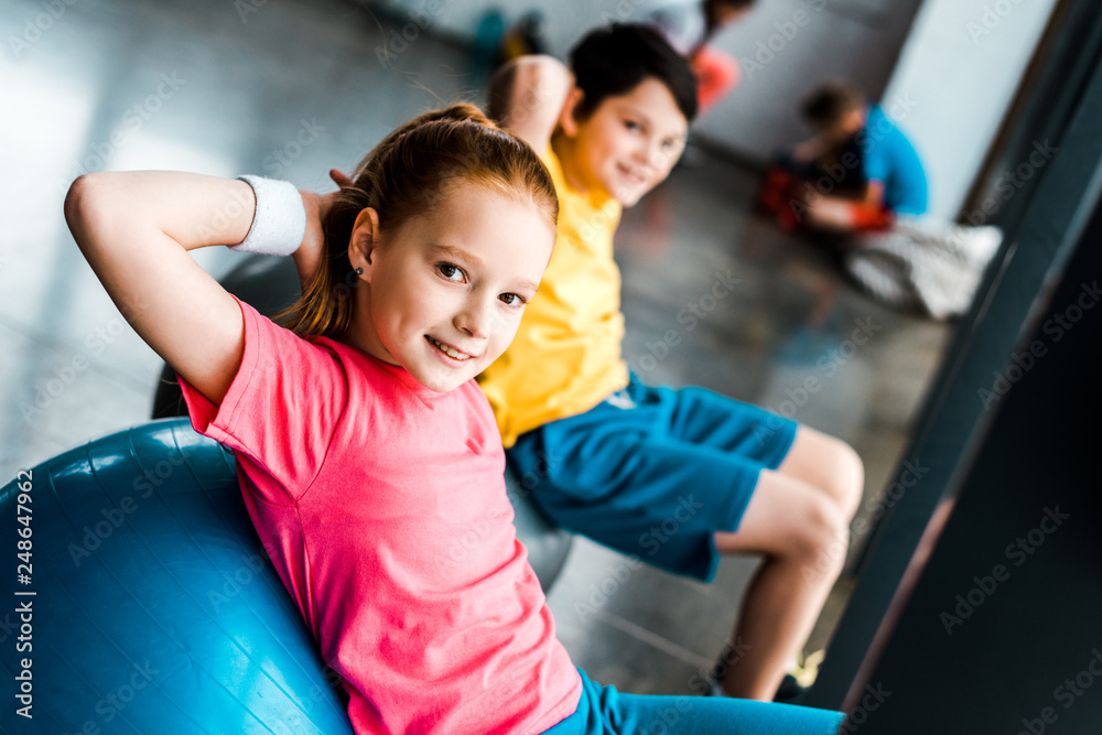Smiling kids doing abs exercise with fitness balls in gym Stock Photo