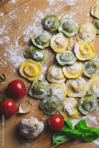 Homemade fresh Italian ravioli pasta on wood table  with flour, basil,tomatoes,background,top view.