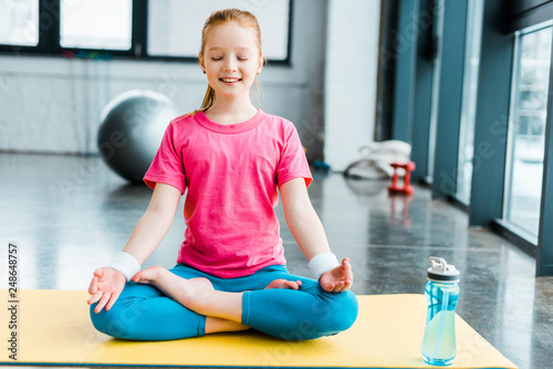 Ginger kid practicing yoga and sitting in lotus pose with closed eyes