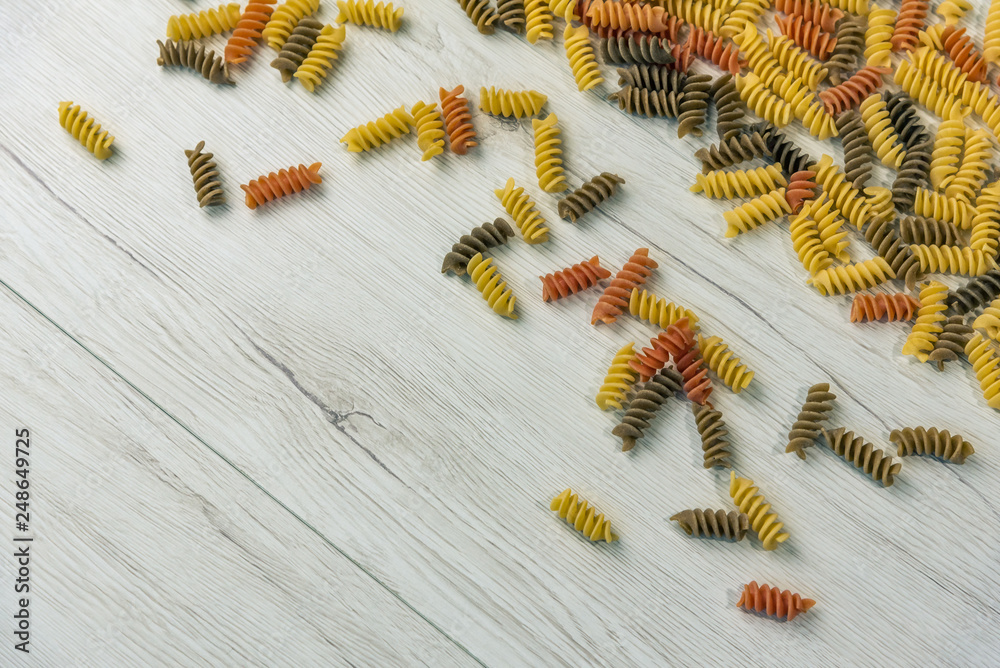 Naklejka premium Raw uncooked three-colored Fusilli on white wood table.