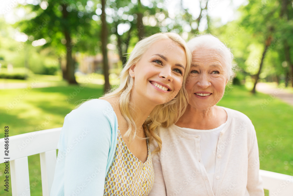 Naklejka premium family, generation and people concept - happy smiling young daughter with senior mother sitting on park bench a