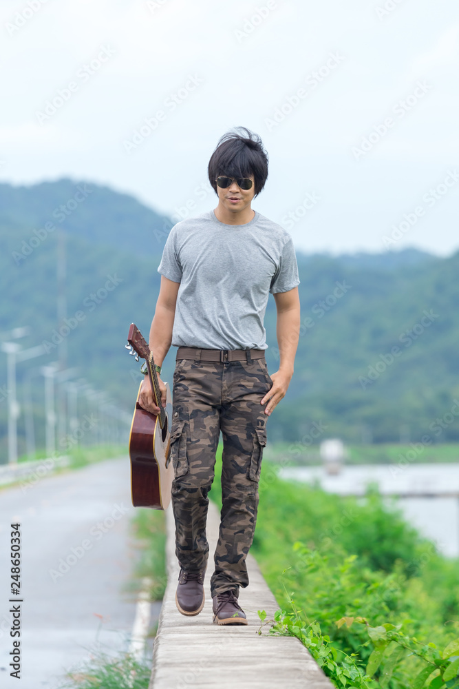 Guy with guitar standing on the dam,  cargo pants