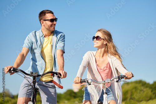 people, leisure and lifestyle concept - happy young couple riding bicycles in summer