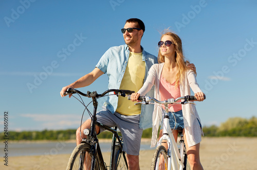 people, leisure and lifestyle concept - happy young couple riding bicycles on beach