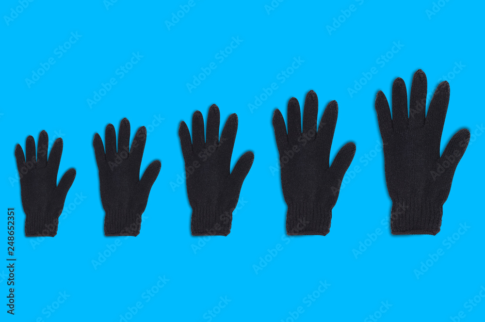 Obraz premium Horizontal row of black warm woolen gloves from small to large on blue background. Top view