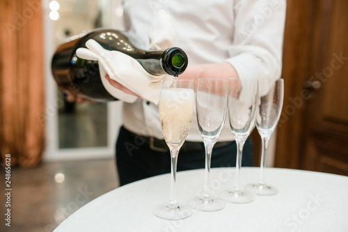 sommelier waiter pours big giant bottle of champagne in a transparent glass on a white table