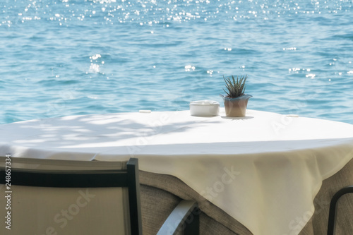 Canvas Print Empty table in a cafe on the shore of the sea or lake, covered with a white tabl