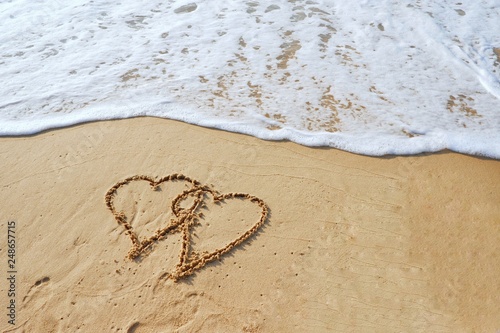 Valentine's day concept, two heart shape drawing on sand beach with ocean background.