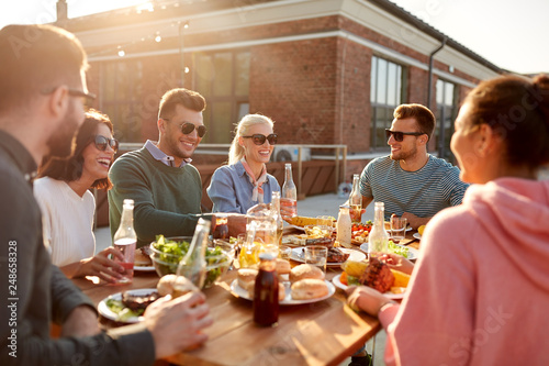 leisure and people concept - happy friends with drinks having dinner or barbecue party on rooftop