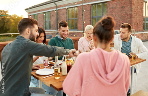 leisure and people concept - happy friends eating at dinner party on rooftop in summer