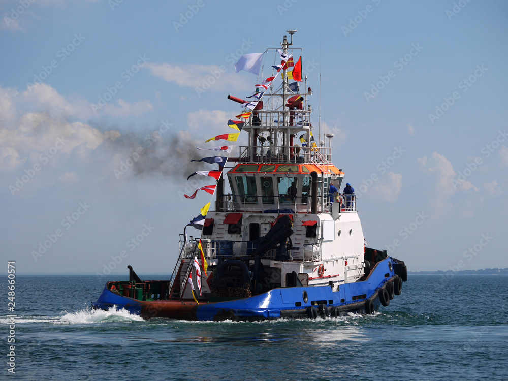 Fototapeta premium Harbour tugboat maneuvering in bay during maritime festival activities.