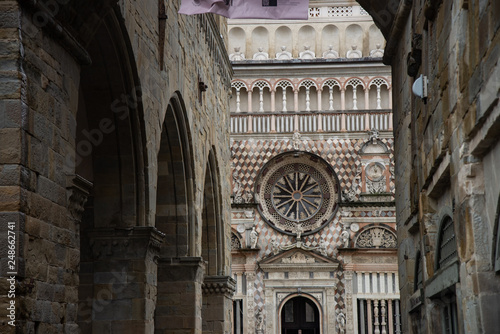 Exterior of the Basilica of St. Mary Major and the Colleoni Chapel. The front facade has a series of polychrome decorations in cream and pink tones. Piazza del Duomo in Bergamo, Italy.