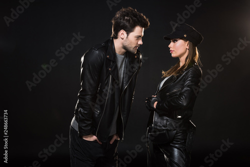 beautiful couple in leather jackets looking at each other and posing on black background