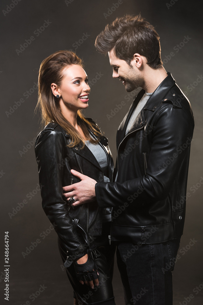 beautiful smiling couple in leather jackets looking at each other and posing on dark background beautiful smiling couple in leather jackets looking at each other and posing on dark background