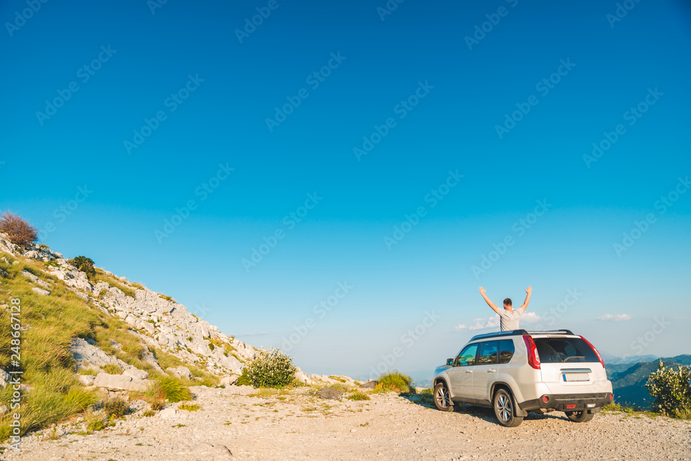 man standing near white suv car on the peak of the hill with beautiful view of mountains. car travel