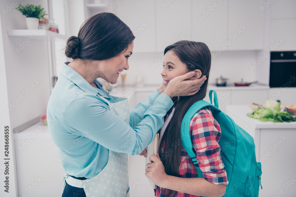 Fototapeta premium Profile side view portrait of two nice cute lovely sweet adorable attractive cheerful cheery positive people kind mom cuddling in light white kitchen interior